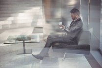 Geschäftsmann hält Einweg-Kaffeetasse in der Hand und hört Musik, während er im Büro auf dem Sofa sitzt — Stockfoto