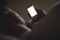 Uomo che usa il suo cellulare mentre si rilassa a letto a casa — Foto stock