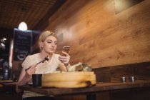 Frau benutzt Handy beim Sushi-Essen im Restaurant — Stockfoto