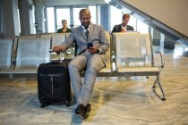 Бизнесмен, пользующийся мобильным телефоном в зоне ожидания в терминале аэропорта — стоковое фото