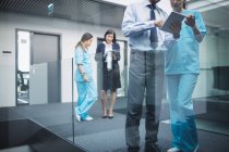 Лікарі та медсестри обговорюють цифровий планшет у лікарняному коридорі — стокове фото