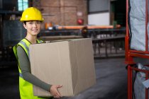 Portrait de belle travailleuse portant une boîte dans un entrepôt — Photo de stock