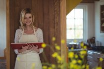 Retrato de mujer hermosa sosteniendo libro de recetas en la puerta de la cocina - foto de stock