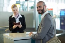 Усміхнений комісар стоїть за лічильником, перевіряючи свій паспорт в терміналі аеропорту — стокове фото