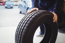 Mid-section of mechanic pushing a tyre in repair garage — Stock Photo