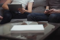 Sezione centrale di due uomini che utilizzano tablet digitale e telefono cellulare in soggiorno a casa — Foto stock