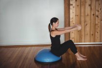 Mid adult woman doing exercise on bosu ball in fitness studio — Stock Photo