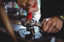 Крупный план официантки, использующей фальсификатор для прессования молотого кофе в портовый фильтр в кафе — стоковое фото