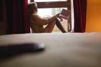 Woman sitting on window and reading a book at home — Stock Photo