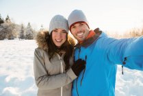 Портрет счастливой пары, делающей селфи на снежном ландшафте — стоковое фото
