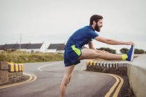 Handsome athlete stretching his leg on the road — Stock Photo