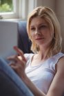 Женщина сидит на диване и пользуется цифровым планшетом в гостиной дома — стоковое фото