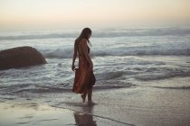 Rückansicht einer Frau, die in der Abenddämmerung am Strand posiert — Stockfoto