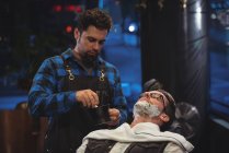 Barbiere applicando crema su barba di cliente in negozio di barbiere — Foto stock