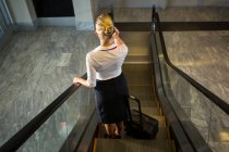 Mitarbeiterinnen mit Gepäck telefonieren auf Rolltreppe im Flughafen — Stockfoto