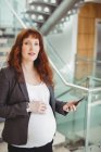 Pregnant businesswoman holding mobile phone near stairs in office — Stock Photo