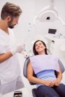 Dentiste parlant avec une patiente souriante allongée sur une chaise à la clinique — Photo de stock