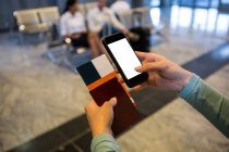 Female hands holding smartphone, passport and boarding pass at airport terminal — Stock Photo