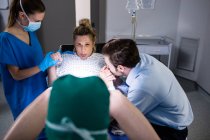 Доктор вивчає вагітну жінку під час пологів, а чоловік тримає руку в операційній кімнаті — стокове фото
