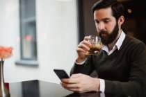 Mann trinkt Glas, während er Handy in Bar benutzt — Stockfoto