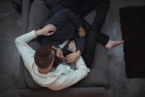 Pareja gay abrazando mientras se relaja en sofá en sala de estar - foto de stock