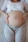 Средняя часть беременной женщины отдыхает на кровати в спальне — стоковое фото