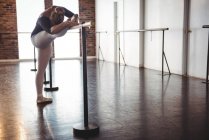Ballerina stretching at barre in ballet studio — Stock Photo
