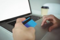 Mujer haciendo el pago en línea utilizando el ordenador portátil y tarjeta de crédito en la cafetería - foto de stock