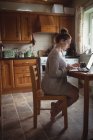 Mulher usando laptop na mesa na cozinha em casa — Fotografia de Stock
