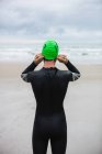 Vista traseira do atleta em terno molhado usando touca de natação na praia — Fotografia de Stock