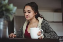 Frau trinkt Kaffee, während sie zu Hause am Laptop arbeitet — Stockfoto