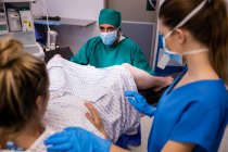 Équipe médicale examinant la femme enceinte pendant l'accouchement en salle d'opération — Photo de stock