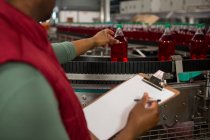 Sección media del trabajador masculino que inspecciona botellas de jugo rojo en la línea de producción en fábrica - foto de stock