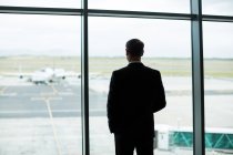Вид ззаду бізнесмена, який дивиться через вікно в зоні очікування в аеропорту — стокове фото