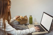 Vista lateral de la mujer usando el ordenador portátil mientras come ensalada - foto de stock
