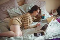Hermosa mujer usando el ordenador portátil mientras toma café en la cama en casa - foto de stock