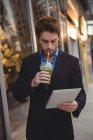 Бизнесмен, использующий цифровой планшет, выпивая сок на улице — стоковое фото