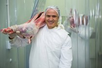 Portrait of butcher carrying raw meat at meat factory — Stock Photo