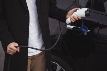 Средняя часть человека держит автомобиль зарядное устройство — стоковое фото