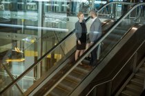 Business people interacting with each other while going up on escalator at airport terminal — Stock Photo