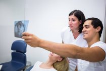 Dentistas discutindo raio-X na frente do paciente na clínica — Fotografia de Stock