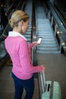 Жінка-комісар з багажем за допомогою мобільного телефону на ескалаторі в аеропорту — стокове фото