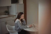 Mulher falando por telefone enquanto usa tablet digital na cozinha em casa — Fotografia de Stock