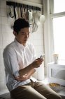 Чоловік використовує мобільний телефон на кухні вдома — стокове фото
