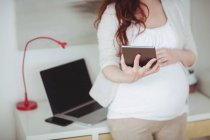 Mittelteil der Schwangeren mit digitalem Tablet im häuslichen Arbeitszimmer — Stockfoto