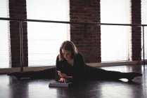 Танцовщица сидит на полу, растягивает и использует цифровой планшет в танцевальной студии — стоковое фото