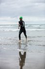 Atleta en traje de neopreno corriendo en la playa - foto de stock
