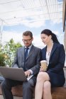 Бизнесмен и коллега сидят снаружи офисного здания и пользуются ноутбуком — стоковое фото