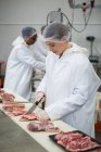 Female butcher cutting meat at meat factory — Stock Photo