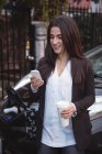 Frau benutzt Handy, während Auto im Hintergrund an Ladestation für Elektrofahrzeuge aufgeladen wird — Stockfoto